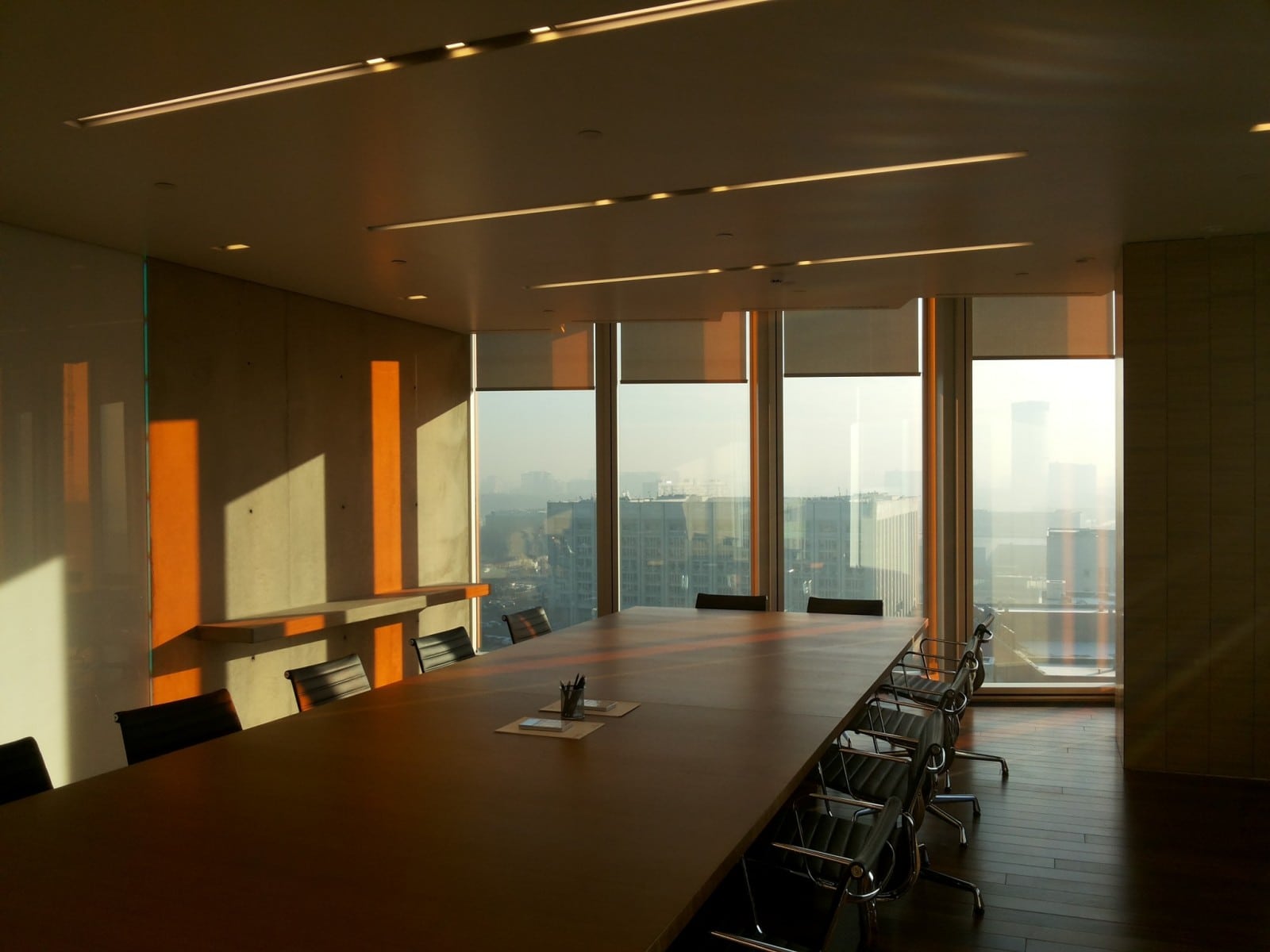 Large office board room with table and chairs beside large floor length windows to increase natural light